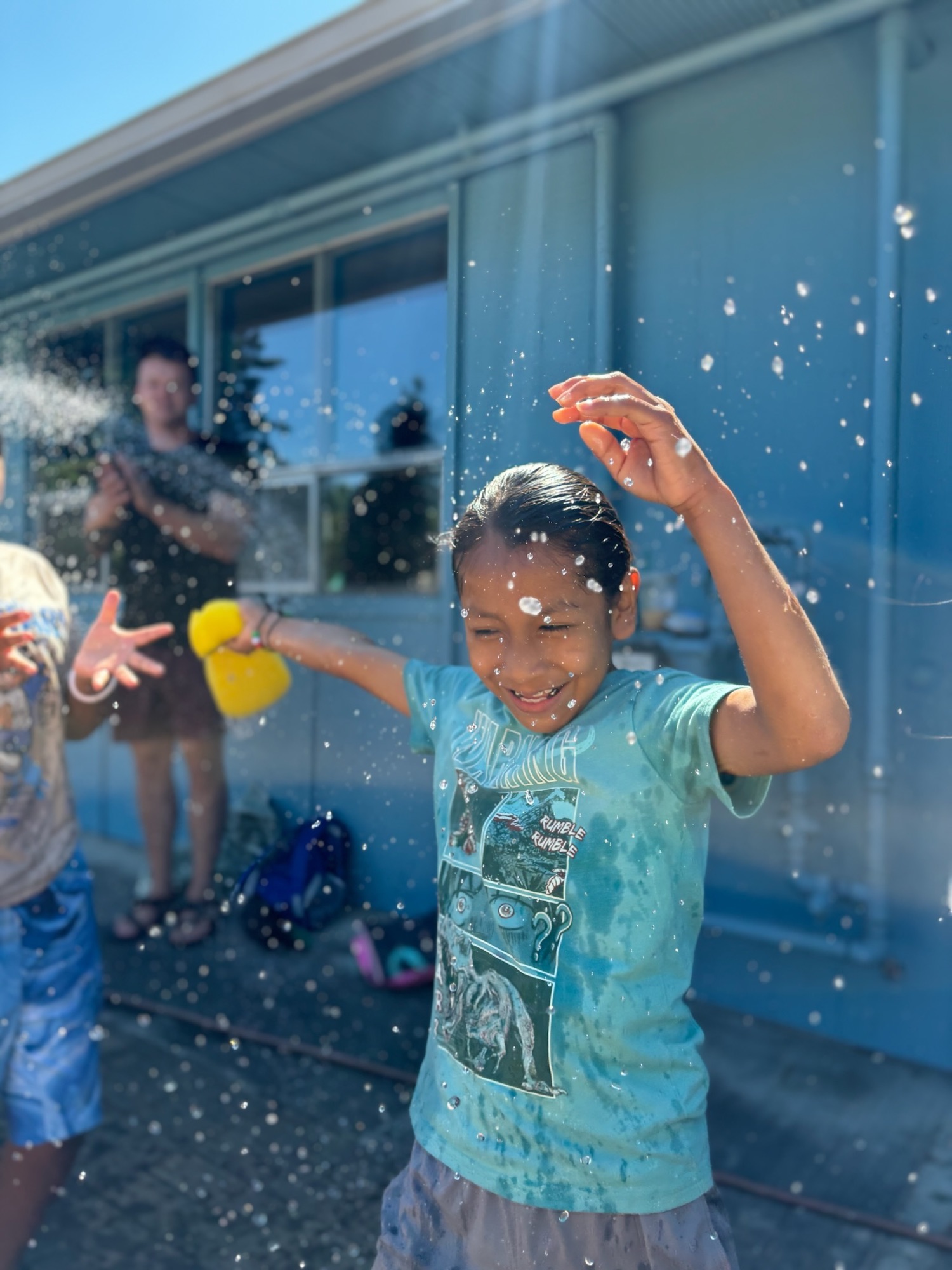 A girl laughing with her arms up in a summer water fight
