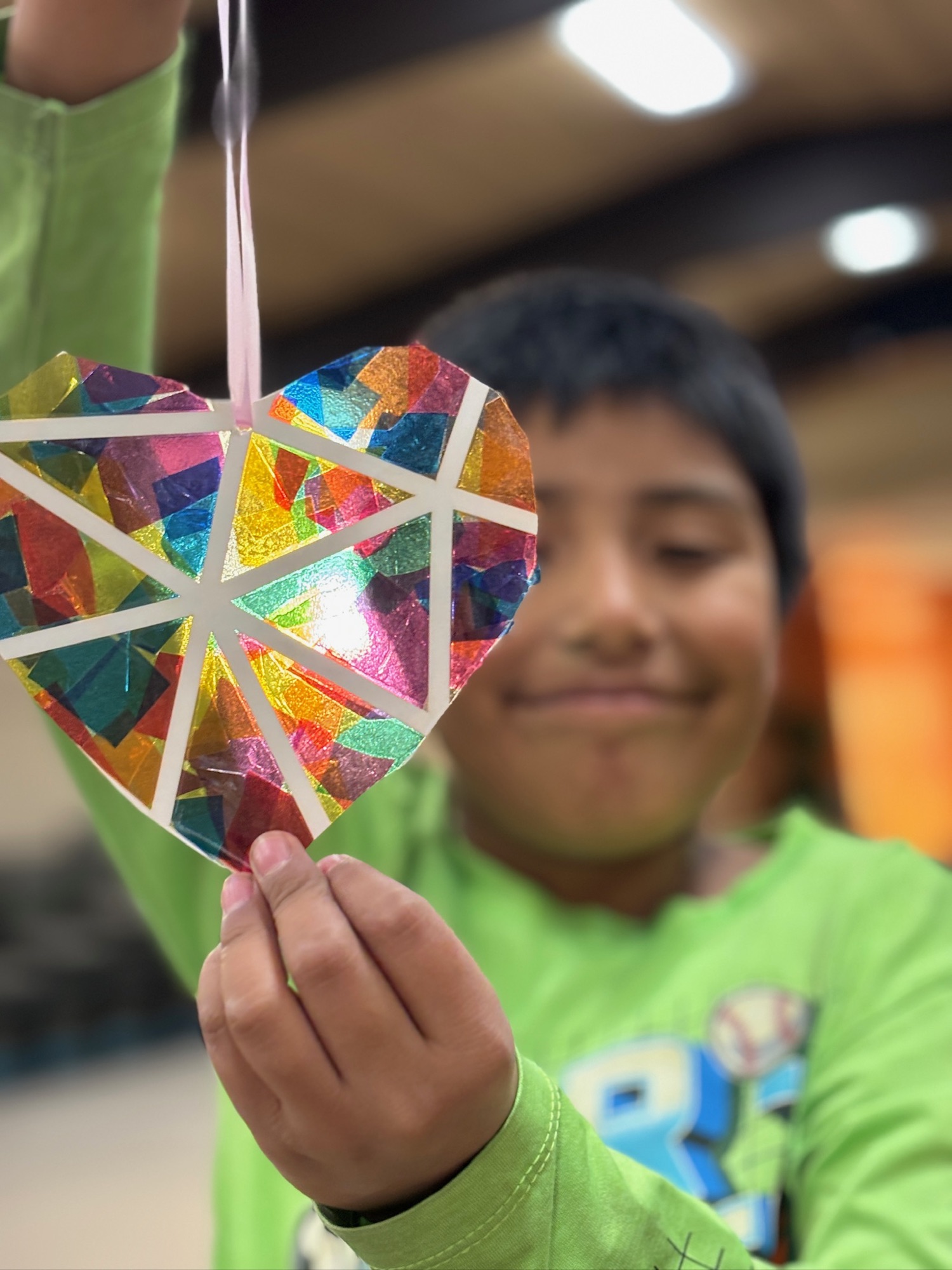 A boy holding up a colorful heart craft he made